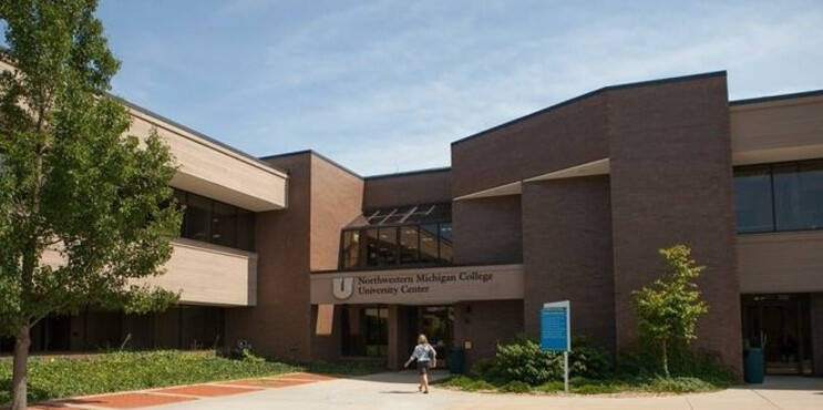 Two-story brown brick academic building with large windows and landscaped entrance.